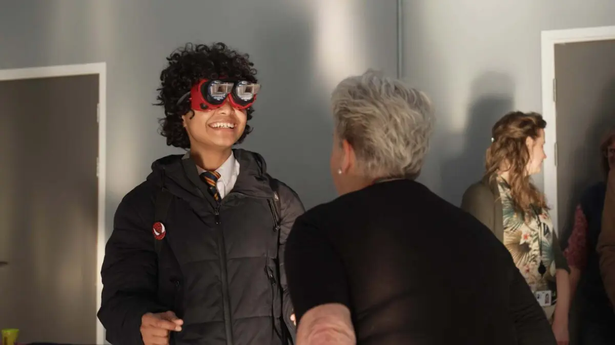 Image of a young boy at a careers fair, he's wearing a type of optometry glasses and smiling